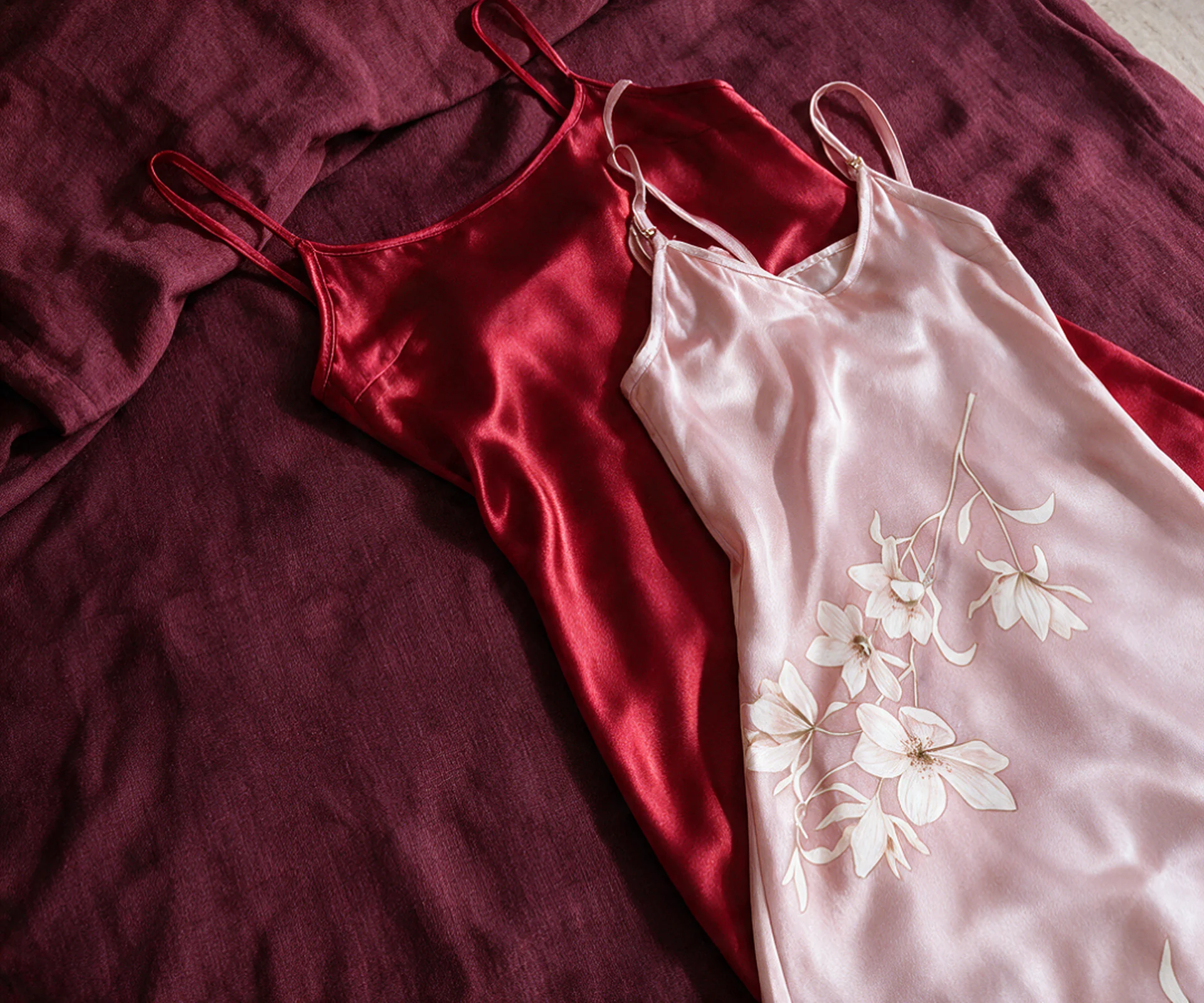 Red satin and pale pink floral slips arranged on wine linen.